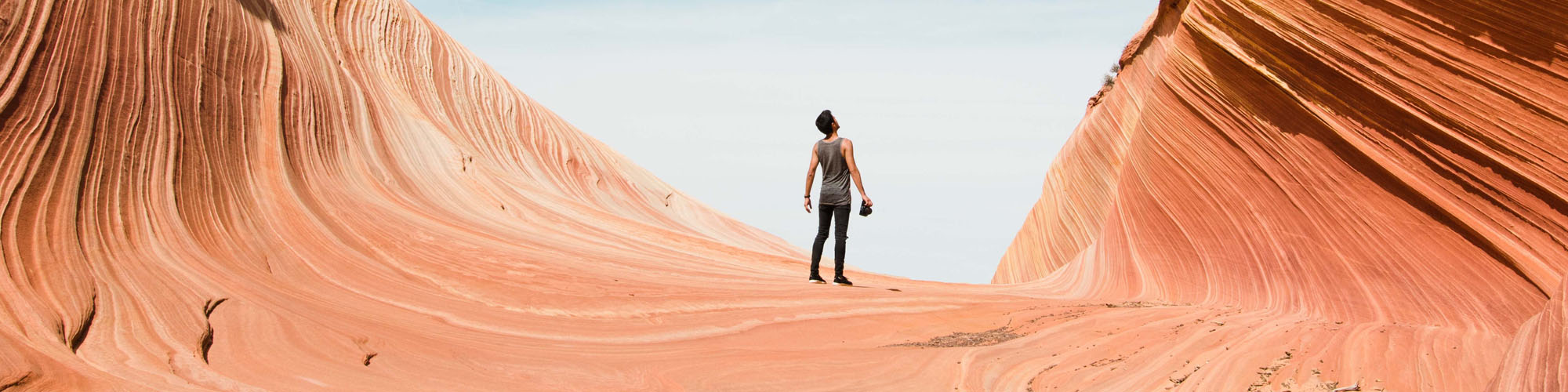 Slot canyon in Utah with clear sky and vibrant earth. One man stands in the distance.