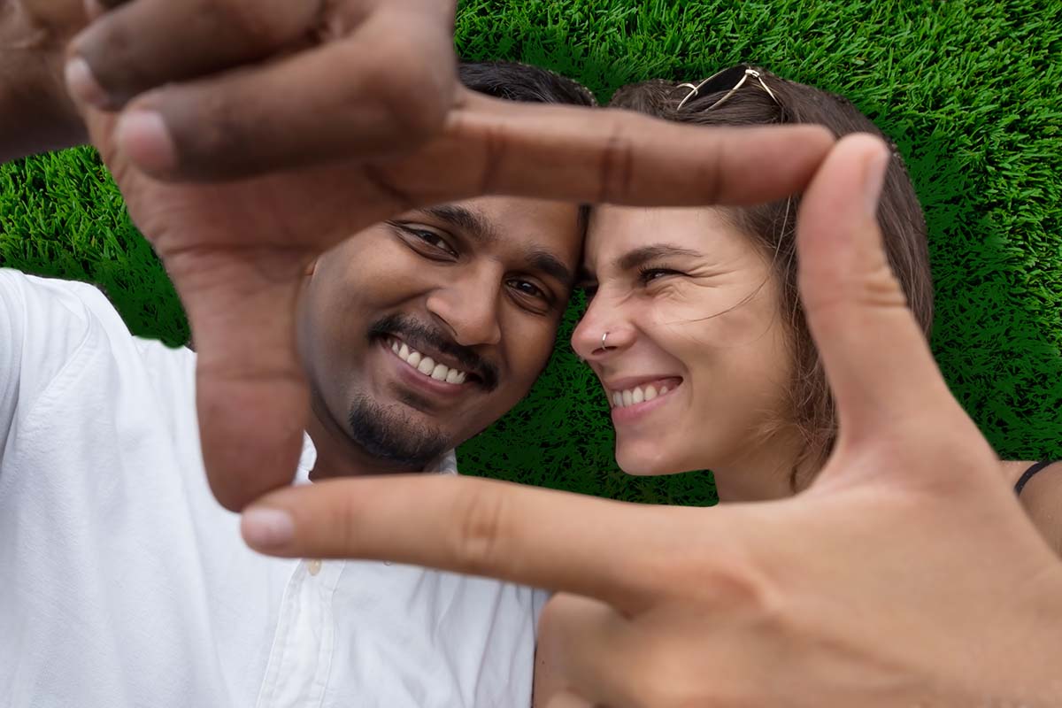 Hispanic man and Caucasian woman laying in the grass smiling at the camera